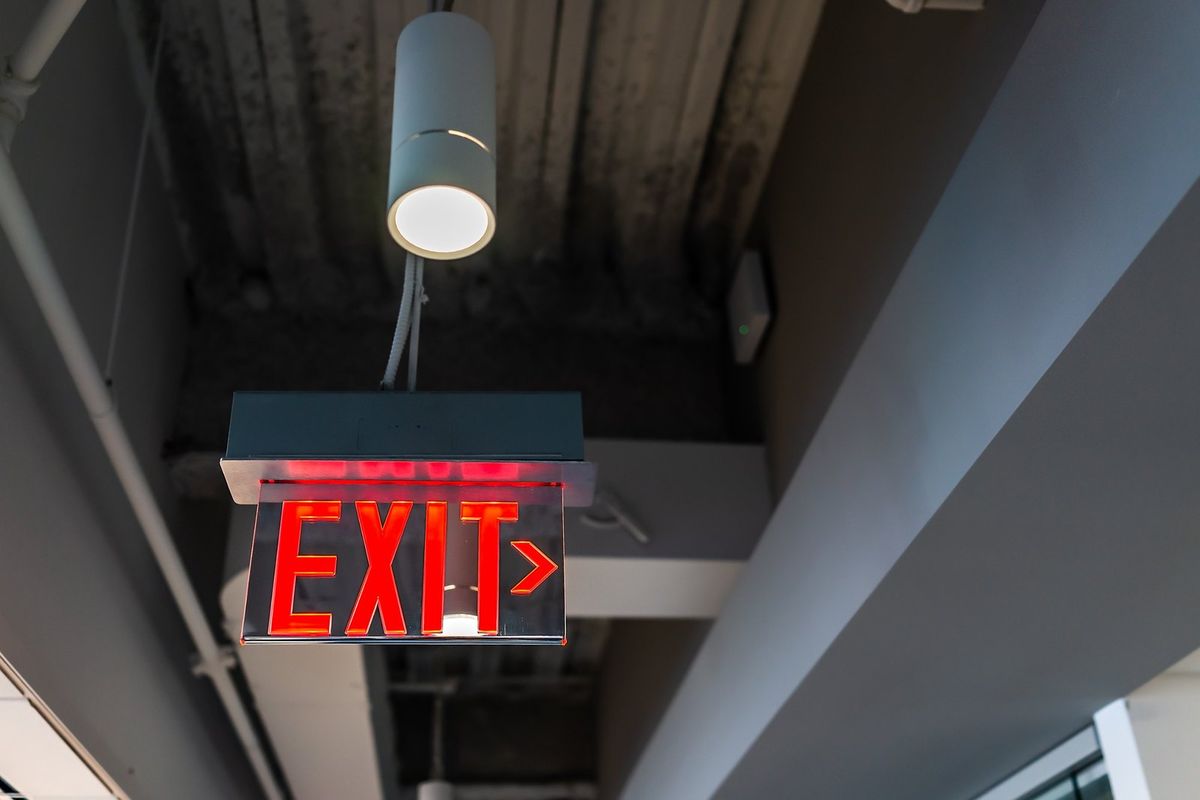 Illuminated red exit sign with a directional arrow hanging from a commercial ceiling